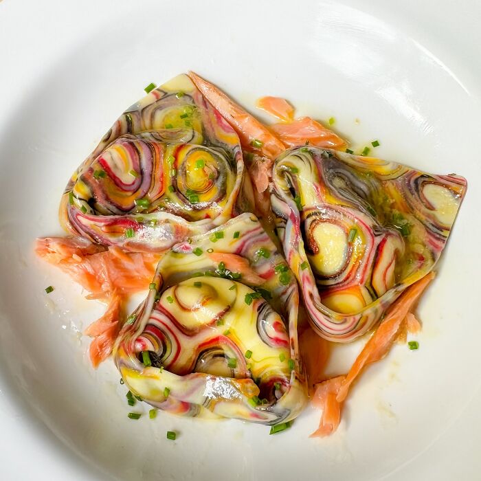 Colorful handcrafted pasta with artistic patterns, garnished with salmon and chives on a white plate.
