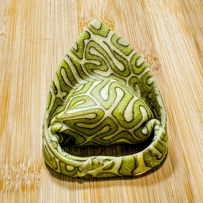 Handcrafted pasta with intricate green patterns on a wooden surface, showcasing culinary artistry.