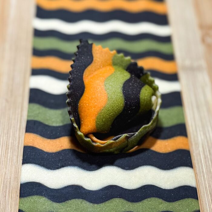 Handcrafted pasta with vibrant wavy patterns in orange, black, and green on a wooden surface.