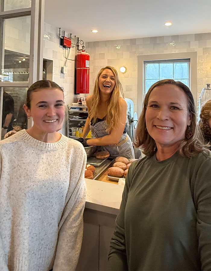 Woman in a striped dress at a donut shop counter, smiling, with donuts in the background. Woman in a striped dress at a donut shop counter, smiling, with donuts in the background.