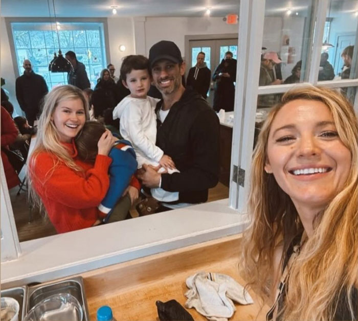 Blonde woman taking a selfie inside a donut shop, smiling with a family in the background. Blonde woman taking a selfie inside a donut shop, smiling with a family in the background.
