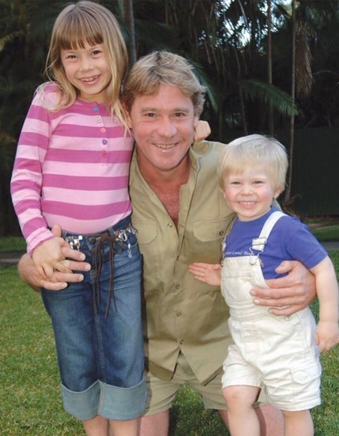 Father with two children outdoors, both smiling and embracing him, in a casual family moment. Father with two children outdoors, both smiling and embracing him, in a casual family moment.