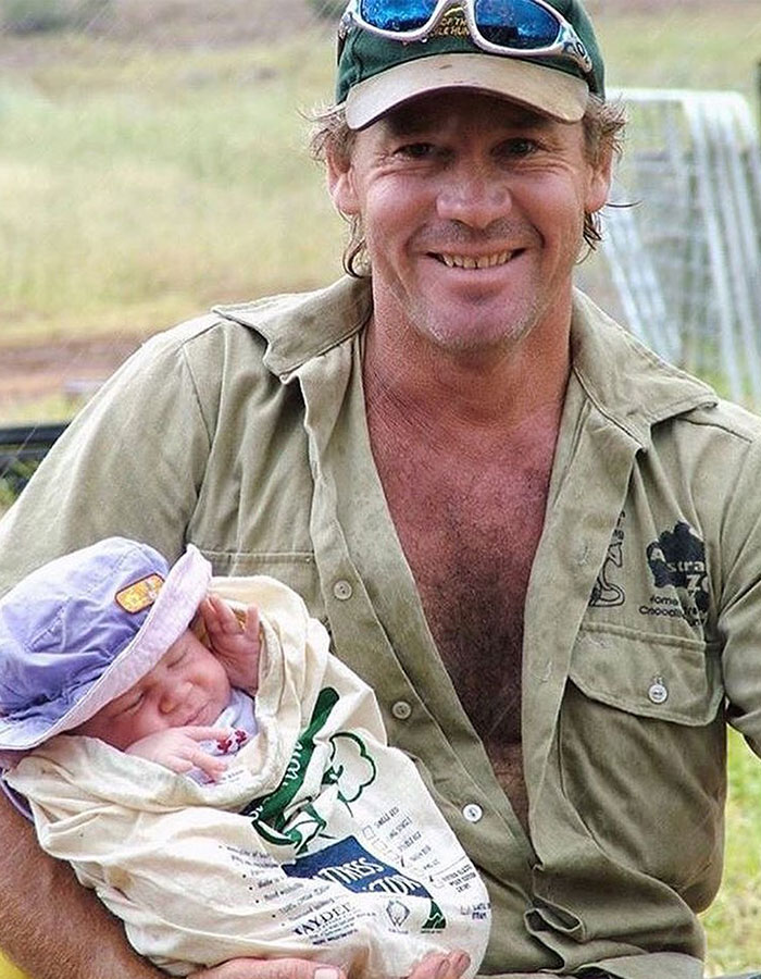 Man smiling in casual attire, holding a newborn swaddled in a cloth. Man smiling in casual attire, holding a newborn swaddled in a cloth.