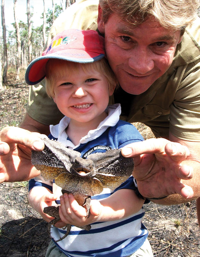 Father and son outdoors holding a frill-necked lizard, showing interest in wildlife exploration. Father and son outdoors holding a frill-necked lizard, showing interest in wildlife exploration.