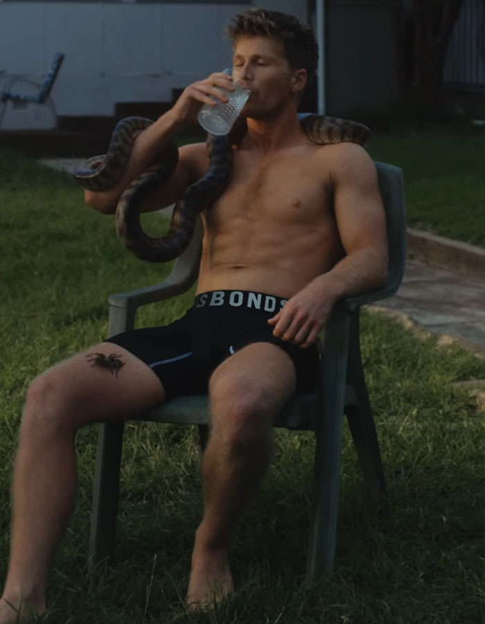 Shirtless man with a snake on his shoulders, sitting outdoors and drinking water. Shirtless man with a snake on his shoulders, sitting outdoors and drinking water.
