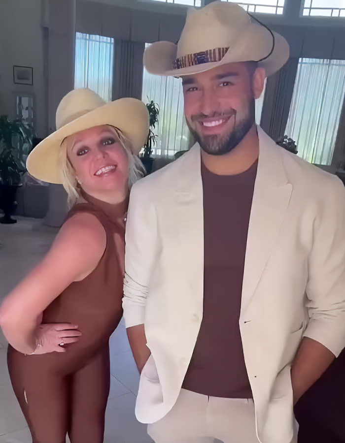 Two people in cowboy hats smiling indoors, one in a brown outfit and the other in a beige suit. Two people in cowboy hats smiling indoors, one in a brown outfit and the other in a beige suit.