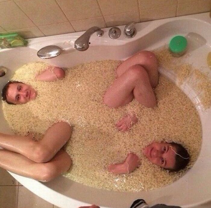 Two people in a bathtub filled with noodles, creating a random cursed image.