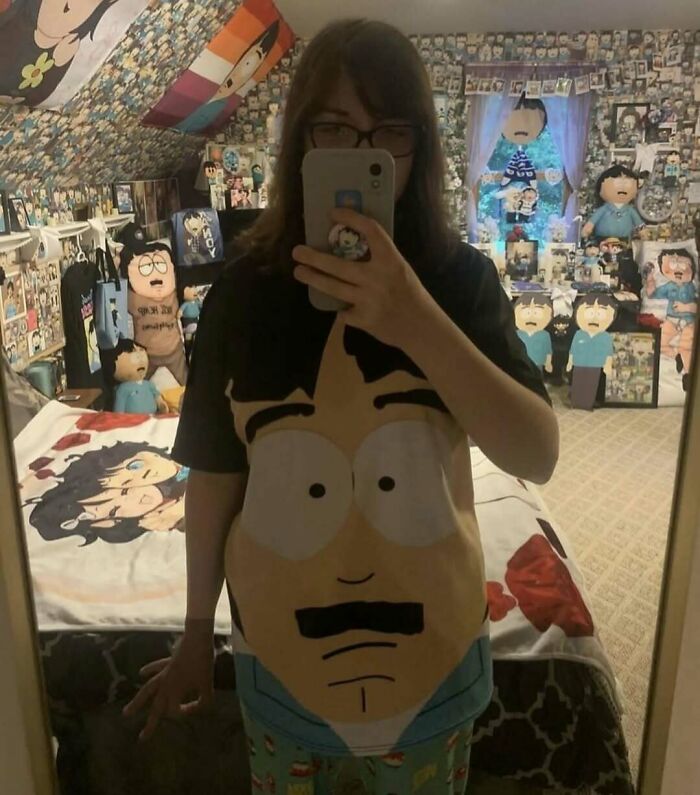 Person in a room full of cartoon-themed decor, taking a mirror selfie, wearing a cartoon face t-shirt. Cursed image vibes.