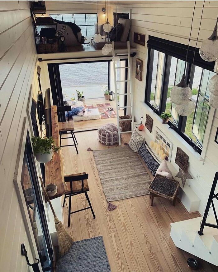 Cozy and clever tiny home interior with loft, natural wood floors, and large windows showcasing off the grid living.
