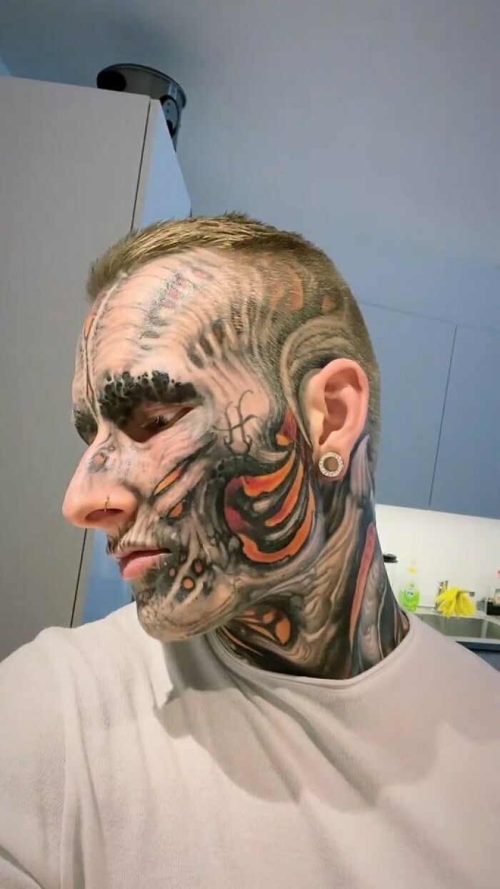 Man with extensive facial tattoos featuring vibrant patterns and designs in a kitchen setting.