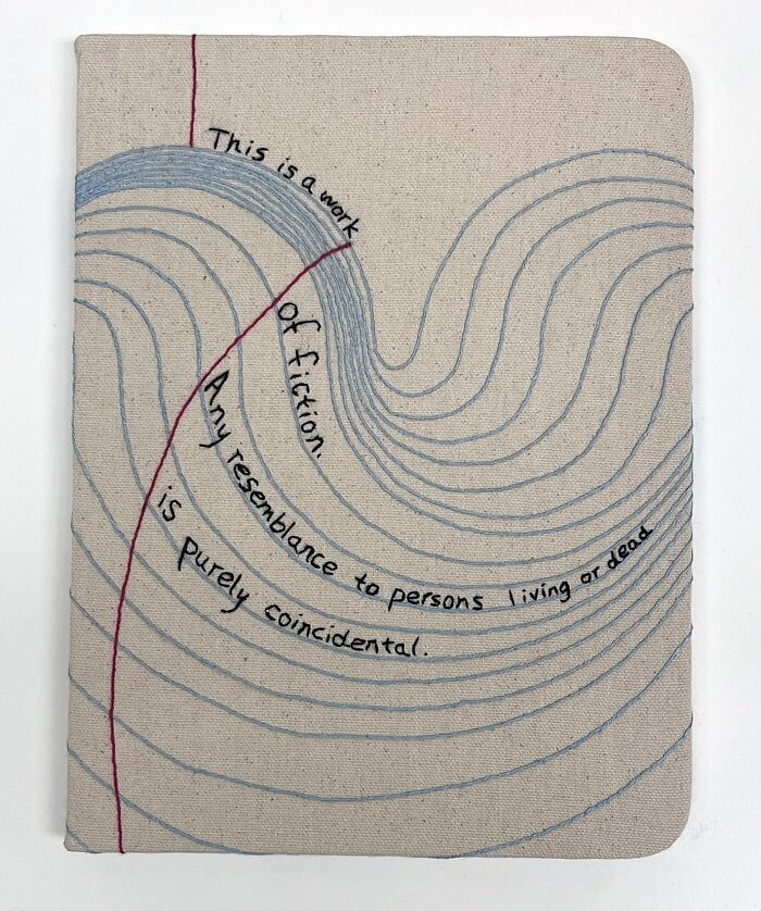Fabric embroidered to resemble a book page with flowing text and curved lines.