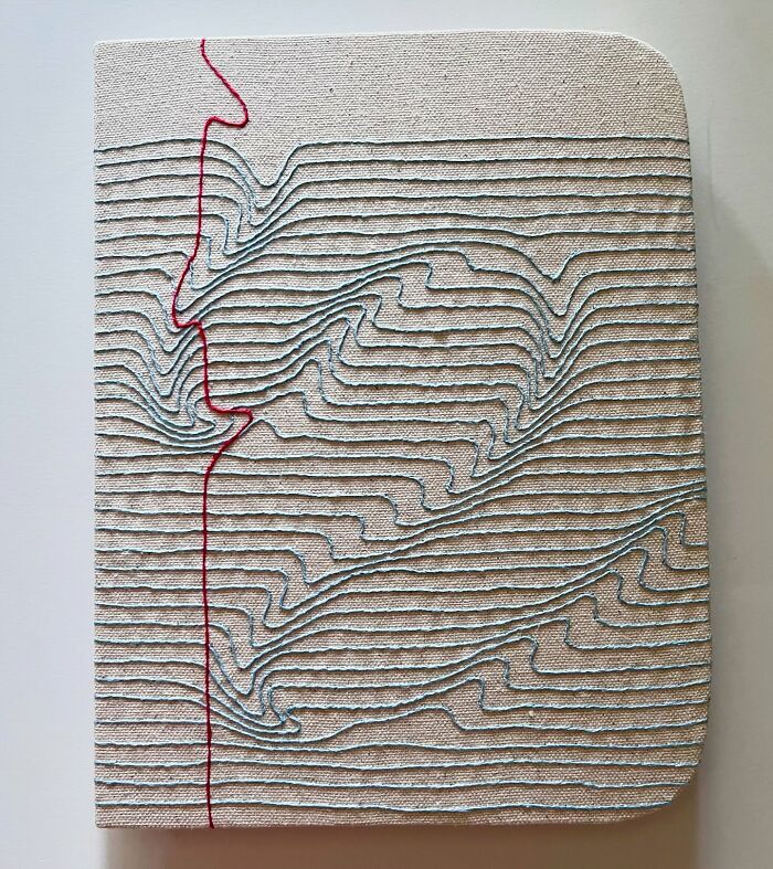 Embroidered fabric resembling notebook pages with flowing line patterns.