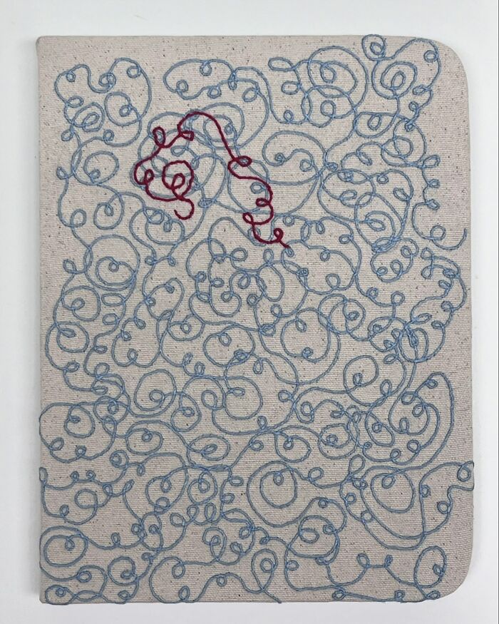 Embroidered fabric mimicking a notebook page, with blue and red thread swirls.