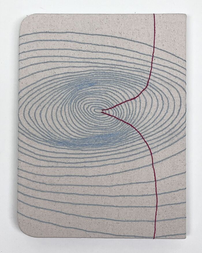 Fabric embroidery resembling notebook pages with intricate spiral design and a red line.