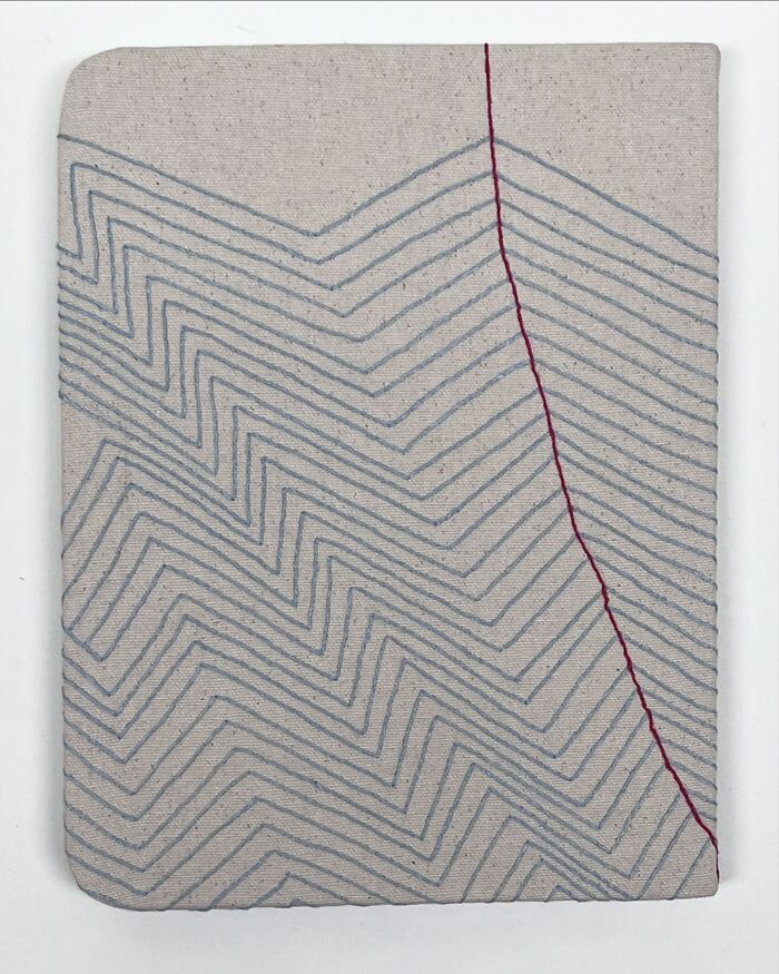 Fabric embroidered to resemble notebook pages with zigzag and vertical lines.