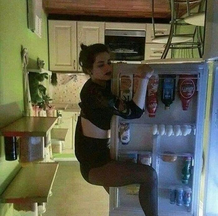 Person hanging on a refrigerator door in an upside-down room, illustrating a random cursed image.