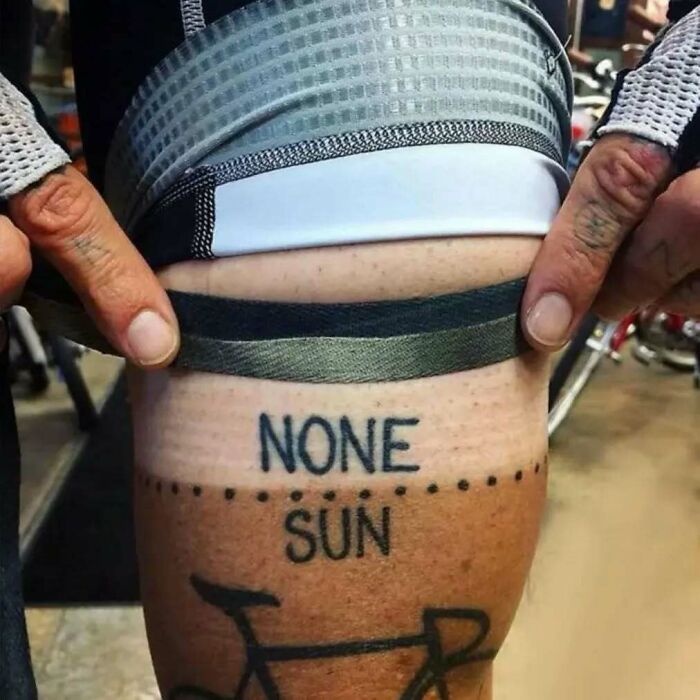 Close-up of a hilariously bad tattoo reading "NONE" above a tan line on a leg.