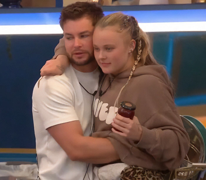 JoJo Siwa embracing a man on Big Brother set, both appearing cozy and relaxed. JoJo Siwa embracing a man on Big Brother set, both appearing cozy and relaxed.