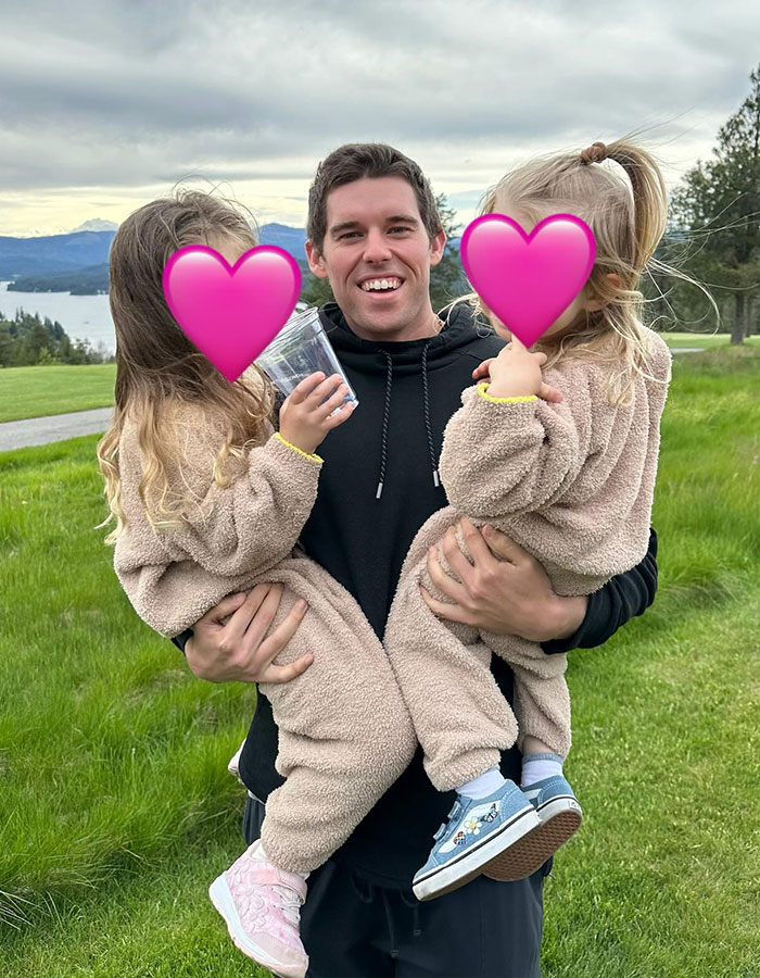 Arnold Schwarzenegger's son smiling outdoors, holding two children with heart emojis on their faces. Arnold Schwarzenegger's son smiling outdoors, holding two children with heart emojis on their faces.