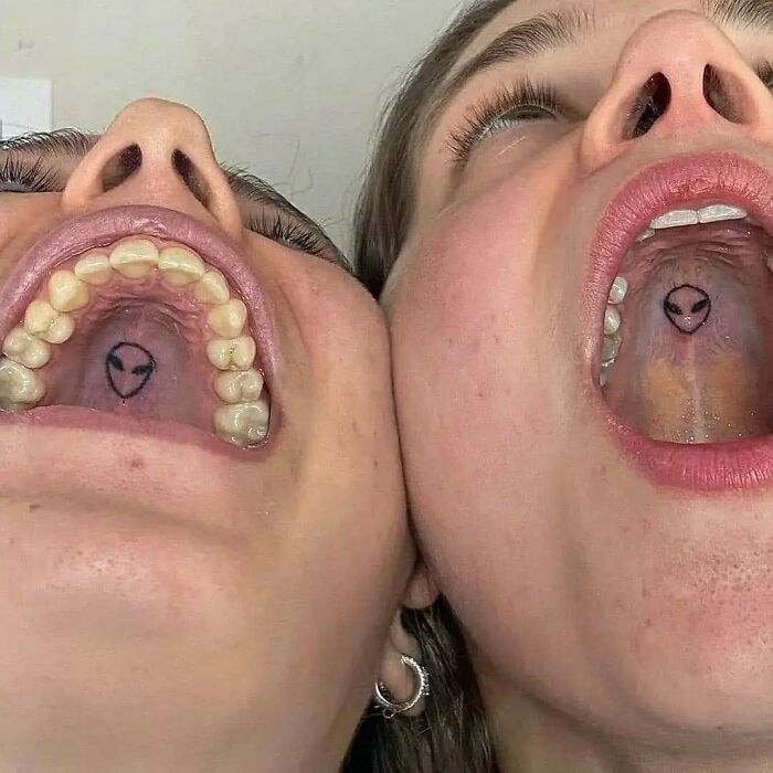Two people showing hilariously bad tattoos of alien faces inside their mouths.