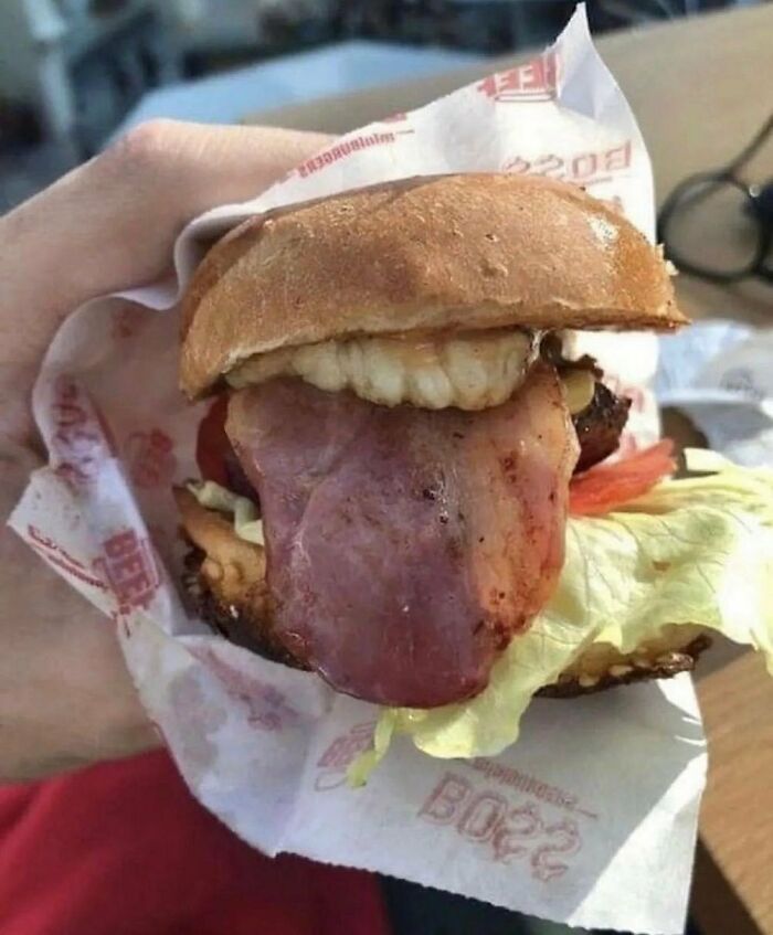Cursed image of a burger with bacon resembling a tongue and something that looks like teeth.