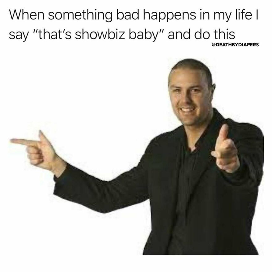 Man in black suit pointing fingers like a finger gun, humorously capturing parenthood chaos and joy.
