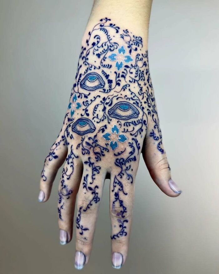 Hand with a blue henna-style tattoo featuring eyes and floral designs, associated with hilariously bad tattoos.
