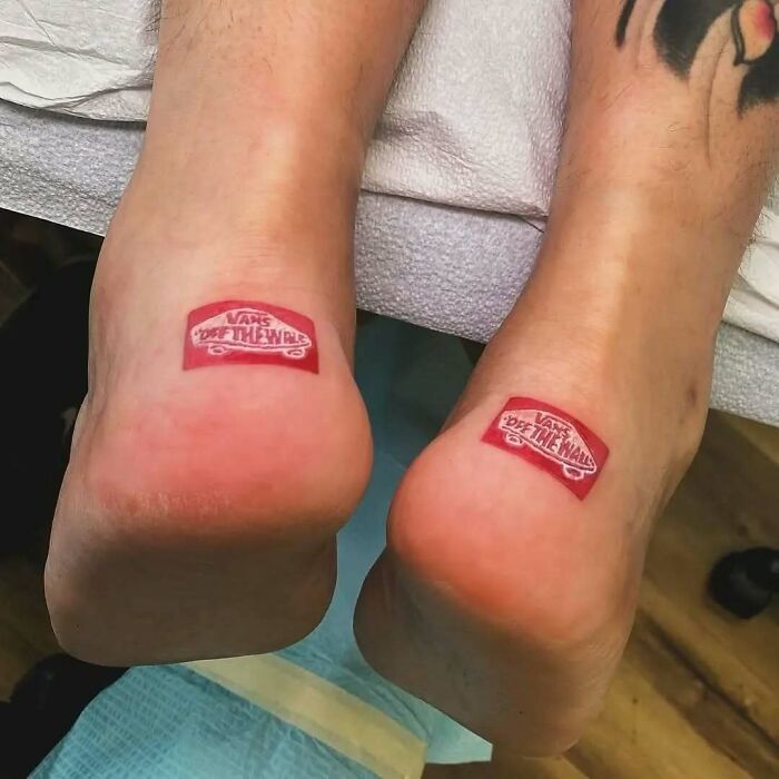 Two feet with hilariously bad tattoo of a red "Vans Off The Wall" logo on each heel.