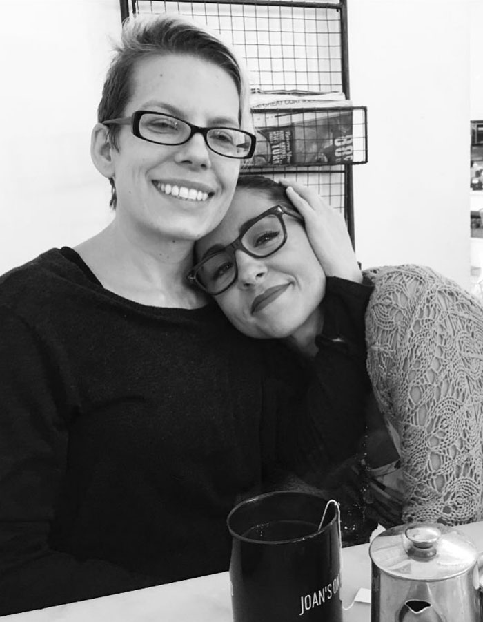 Two women smiling and embracing in a cafe, with a mug labeled "Joan's" on the table in front of them. Two women smiling and embracing in a cafe, with a mug labeled "Joan's" on the table in front of them.