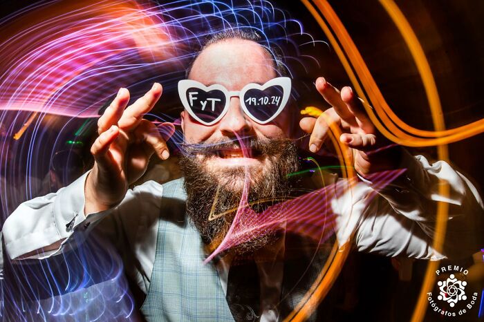 Bearded man in heart-shaped glasses with colorful streaks, capturing wedding celebration vibes.