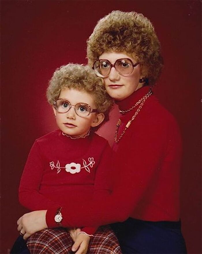 Mother and child with vintage hairstyles and glasses, wearing matching red outfits against a retro backdrop.