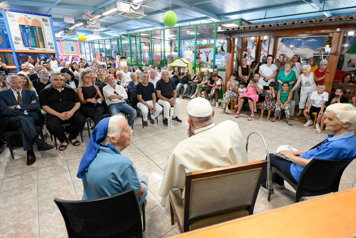 A nun in blue and a religious leader speak to an attentive audience in a colorful meeting room. A nun in blue and a religious leader speak to an attentive audience in a colorful meeting room.