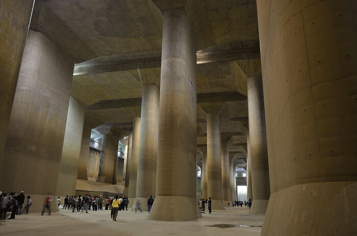 Underground city with massive concrete pillars and people exploring the vast space.