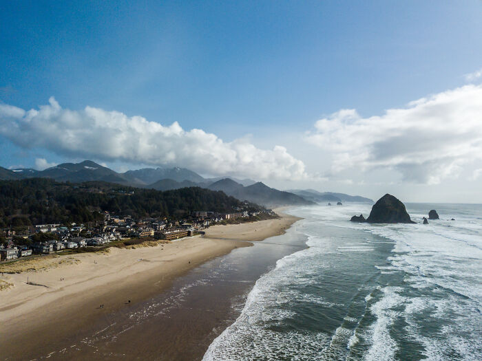 Incredible coastal vista with a sandy beach, ocean waves, and dramatic rock formations under a cloudy sky.