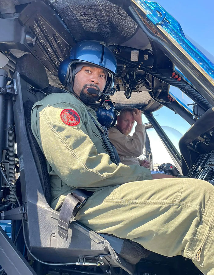 Former Navy SEAL in helicopter cockpit, wearing a helmet, with co-pilot in background. Former Navy SEAL in helicopter cockpit, wearing a helmet, with co-pilot in background.