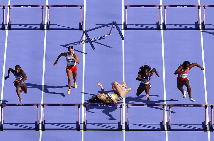 Athletes compete in a hurdle race, with one mid-fall, capturing powerful emotion, Istanbul Photo Awards.
