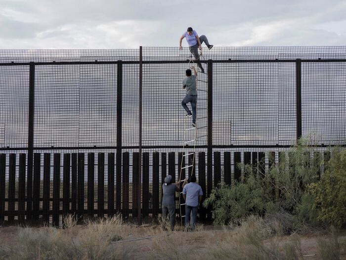 People climbing a border fence using a ladder in a winning Istanbul Photo Awards 2025 image.