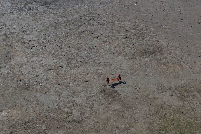 Aerial view of two people holding a stretcher on c*****d earth, illustrating a powerful moment in Istanbul Photo Awards 2025.