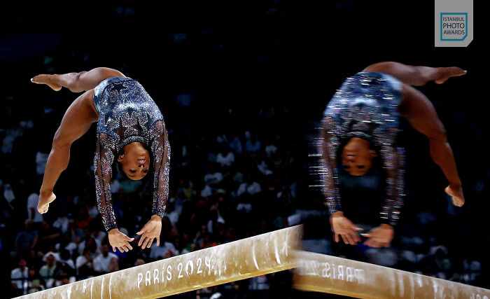 Gymnast performing a backflip on the beam at Paris 2024, showcasing power and grace. Istanbul Photo Awards.