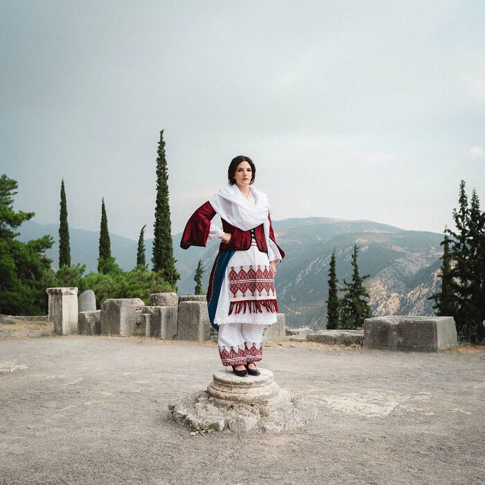 Woman in traditional attire stands on a stone pedestal with mountains in the background, Istanbul Photo Awards 2025.