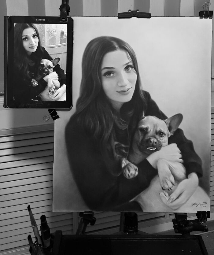 Hyper-realistic pencil portrait of a woman holding a dog, displayed alongside the reference photo on a tablet.