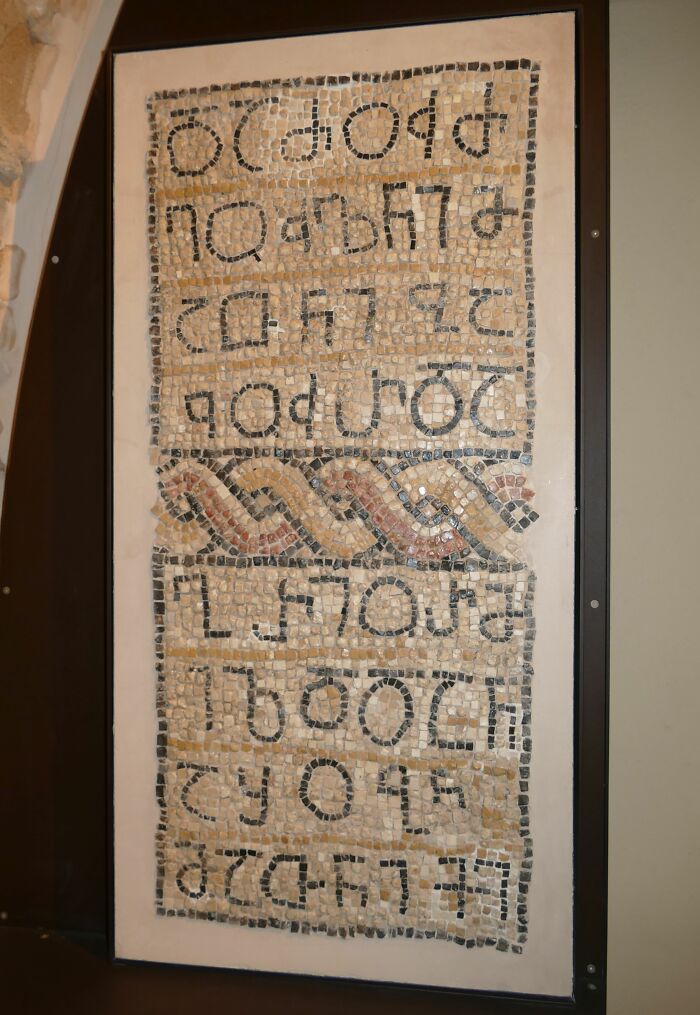 Ancient mosaic text panel displayed upright with decorative patterns, featuring one of the oldest surviving written texts.