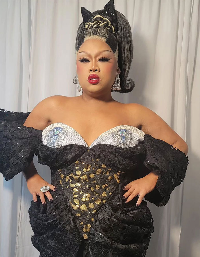 Drag Race alum in an elegant black and gold gown, posing confidently with bold makeup and a stylish updo. Drag Race alum in an elegant black and gold gown, posing confidently with bold makeup and a stylish updo.