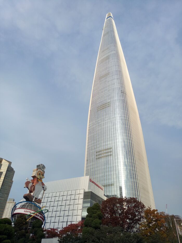 Tall skyscraper reaching into a clear sky, representing one of the world's tallest buildings, with autumn trees below.