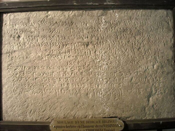 Ancient carved stone with one of the world's oldest written texts, featuring bilingual inscriptions in a museum display.