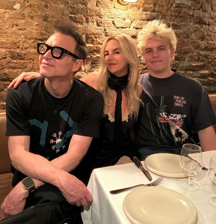 Mark Hoppus from Blink-182 sitting at a dining table with two others, brick wall background. Mark Hoppus from Blink-182 sitting at a dining table with two others, brick wall background.