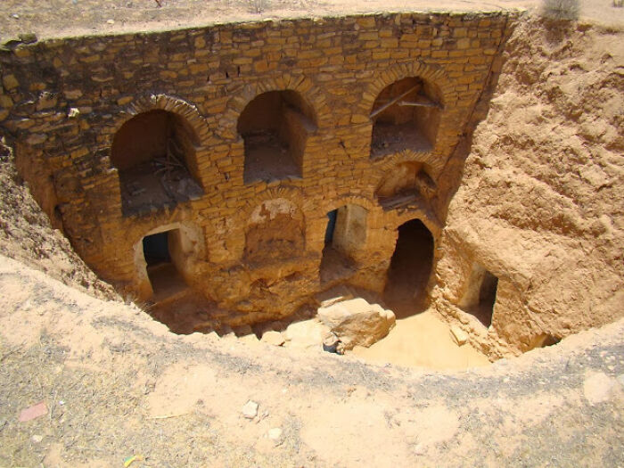 Ancient structure in an eerie underground city, showcasing arched stone entryways and sandy surroundings.