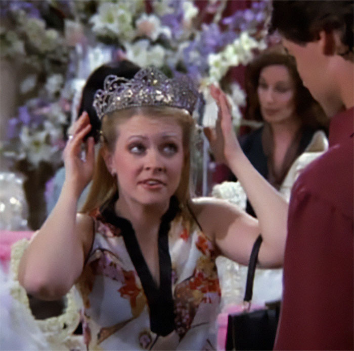 Woman adjusting a tiara at an event, surrounded by floral decorations. Woman adjusting a tiara at an event, surrounded by floral decorations.