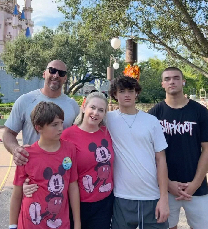 Family posing at a theme park, woman in a red Mickey shirt, castle backdrop, includes "Blink-182" and "Melissa Joan Hart". Family posing at a theme park, woman in a red Mickey shirt, castle backdrop, includes "Blink-182" and "Melissa Joan Hart".