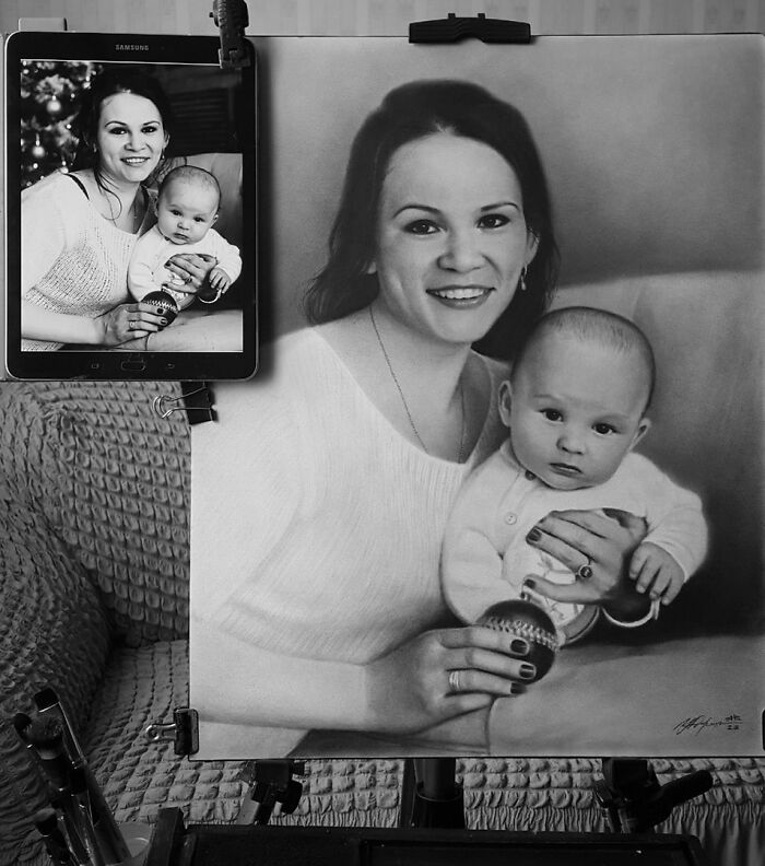A hyper-realistic pencil portrait of a woman and baby, with the original reference photo displayed on a tablet.